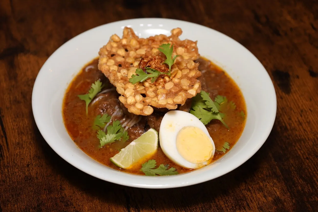 A bowl of mohinga: rice noodles in lemongrass fish soup, topped with a crisp fritter, a boiled egg and coriander